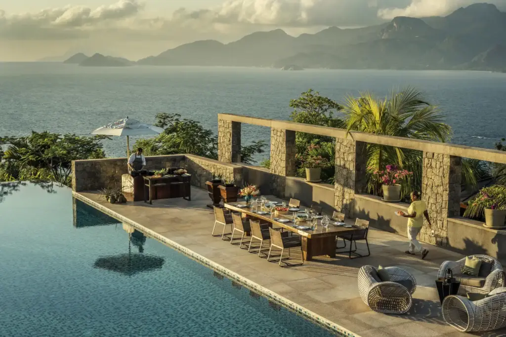 Festlich gedeckte Tafel am Pool des Four Seasons Resort Seychelles, im Hintergrund ferne Bergketten und der weite Indische Ozean. Sie planen eine Hochzeit oder ein festliches Event auf den Seychellen? Katharina Fenners gestaltet den perfekten Aufenthalt, auch für große Gruppen.