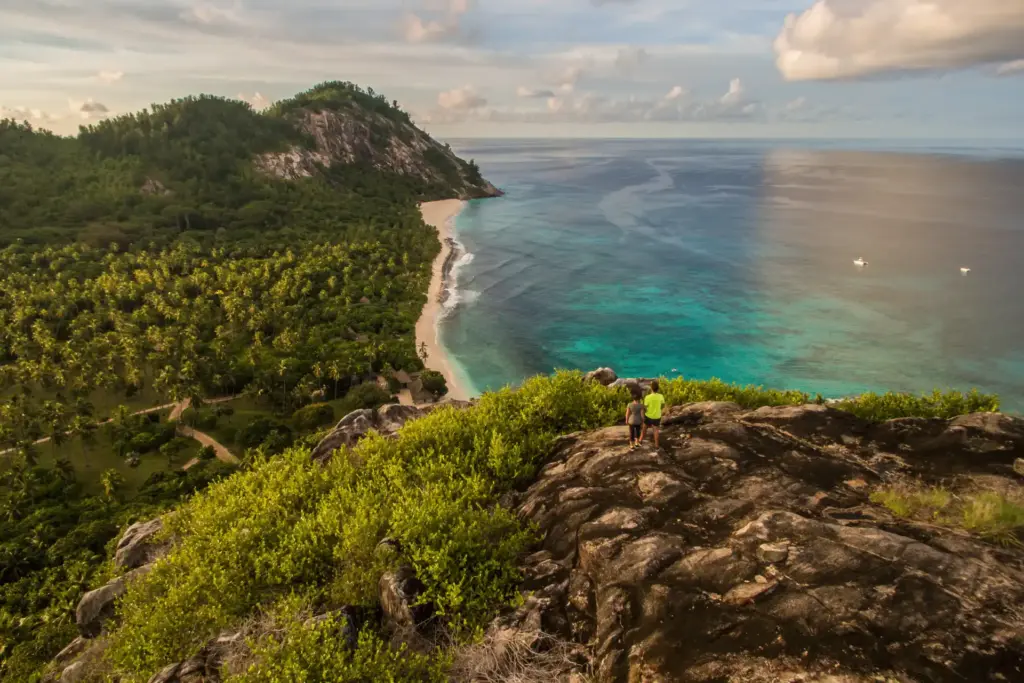 Wanderer auf einer Bergkuppe mit phänomenaler Aussicht über den weiten Indischen Ozean, tief unten, zwischen tropischem Grün, zieht sich ein strahlend weißer Strand ins Endlose. Ein Luxusurlaub auf den Seychellen bietet auch Aktivurlaubern jede Menge Abwechslung in atemberaubender Natur. Katharina Fenners berät Sie individuell und organisiert Ihren maßgeschneiderten Aktivurlaub auf den Seychellen!