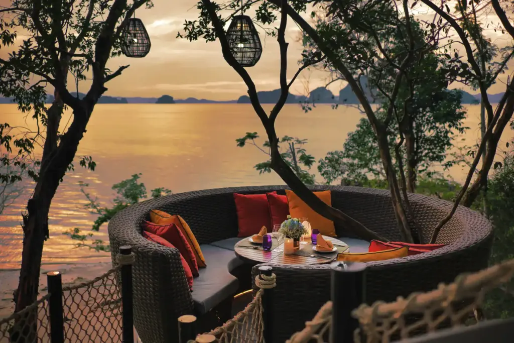 Eine Sitzecke hoch zwischen den Baumkronen, mit weitem Blick über die im Sonnenuntergang golden glänzende Andamanensee - ein Dinner im Bird's Nest des Banyan Tree Krabi ist ein unvergessliches Highlight Ihrer Thailand Luxusreise, buchbar bei Fenners Reisen.