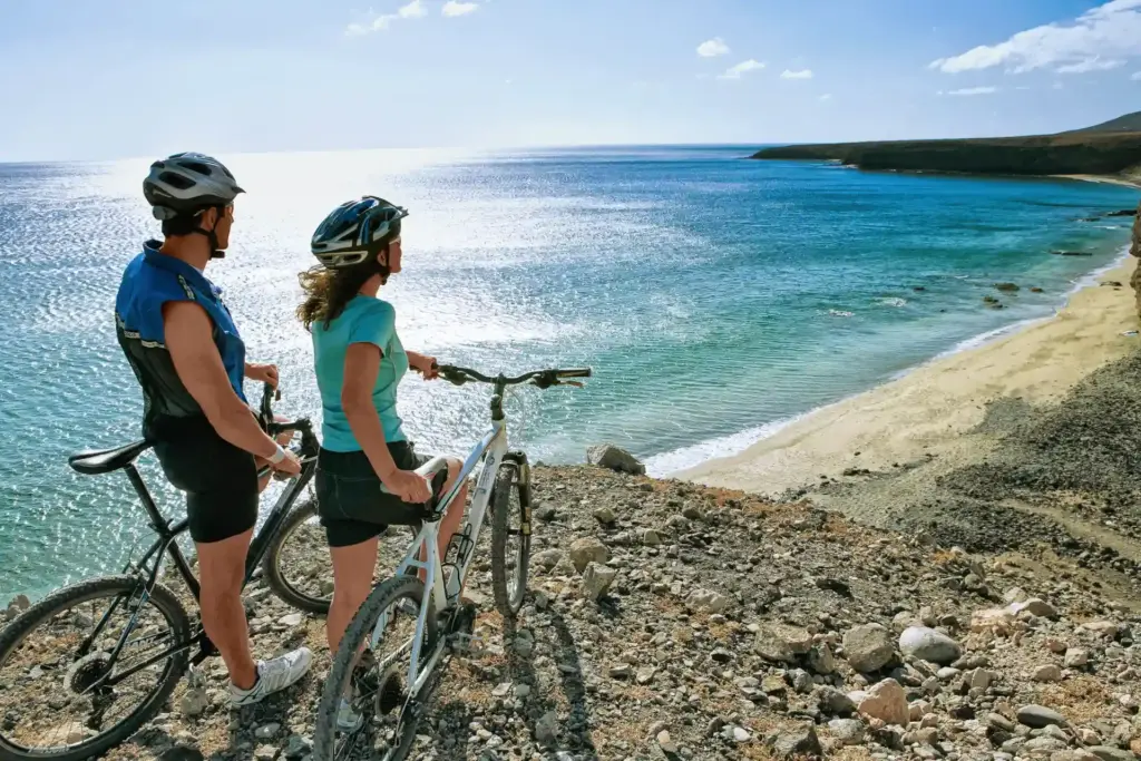 Zwei Radfahrer betrachten den langen Sandstrand unterhalb des Aldiana Club Resorts Fuerteventura, das bei Fenners Reisen gebucht werden kann