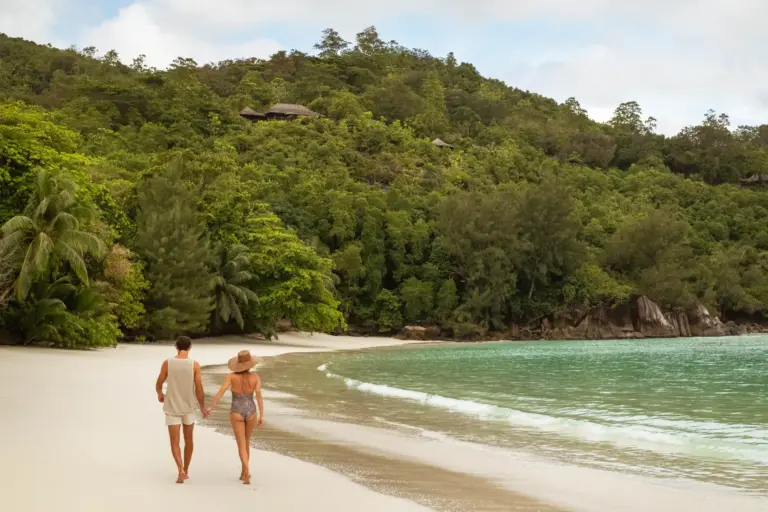 Ein Paar spaziert über einen endlosen Strand - die paradiesische Kulisse der Seychellen bietet sich für unvergessliche Trauungen und Hochzeitsreisen an. Buchen Sie Ihre Seychellen Hochzeitsreise bei den Experten von Fenners Reisen!