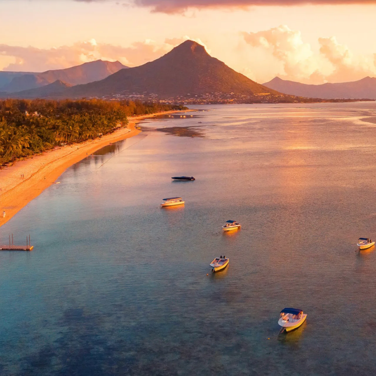 Blick auf den langen Sandstrand vor dem Berg Le Morne, kleine Schiffe schaukeln auf dem golden im Sonnenuntergang leuchtenden Indischen Ozean - Eindrücke einer besonderen Mauritiusreise zum Hochzeitsjubiläum, arrangiert von Fenners Reisen