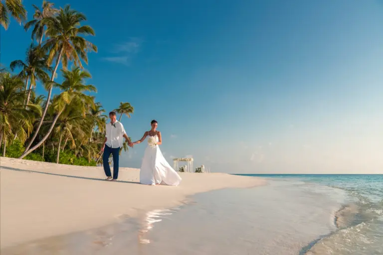 Feinsandiger Strand, türkises Meer, Palmen - ein Hochzeitspaar spaziert über einen Traumstrand wie aus dem Bilderbuch. Buchen Sie exklusive Hochzeitsreisen bei Fenners Reisen, oder planen Sie mit Katharina Fenners Hilfe Ihre Traumhochzeit im Paradies!