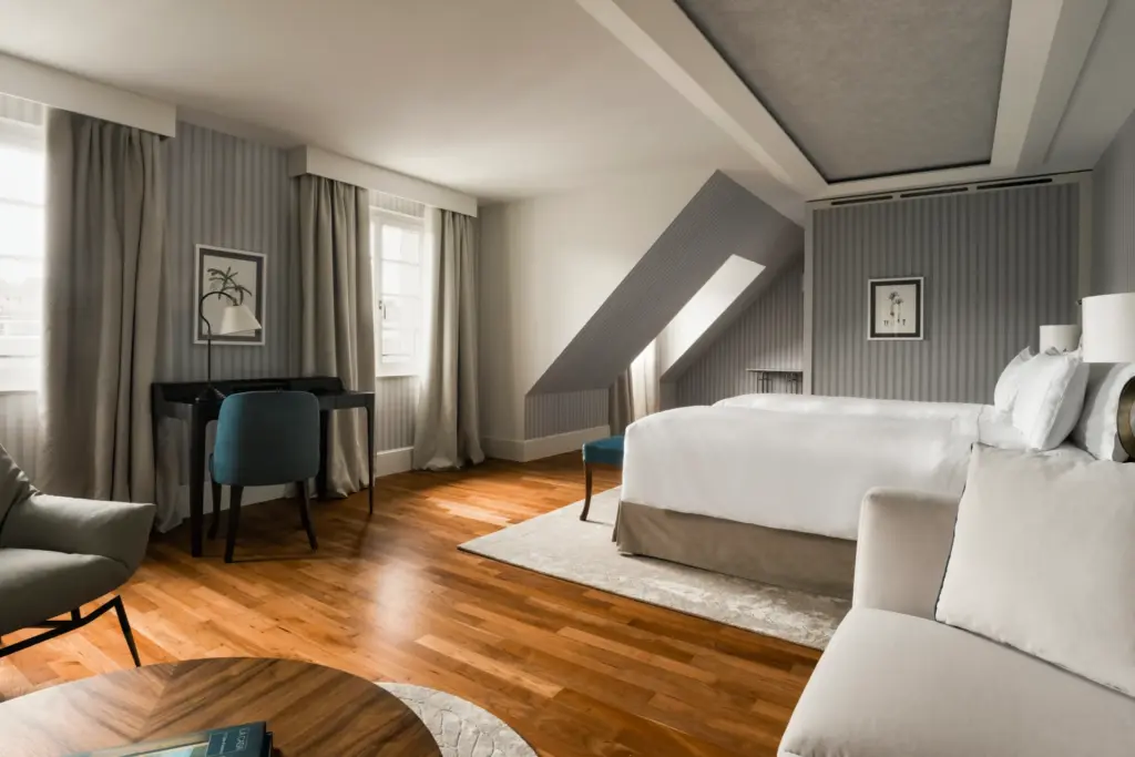 Blick in ein geräumiges Hotelzimmer, es dominieren helle Nuancen, natürliche Materialien und moderne Akzente. So sehen die Deluxe Zimmer im Chenot Palace Weggis aus, buchbar bei Fenners Reisen