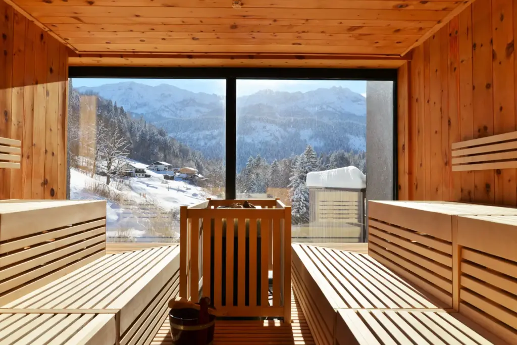 Saune mit großen Glasfronten, aus denen der Blick auf eine verschneite Berglandschaft schweift - der Wellnessbereich des bei Fenners Reisen buchbaren Boutiquehotels DAS GRASECK lädt zum Abschalten ein.