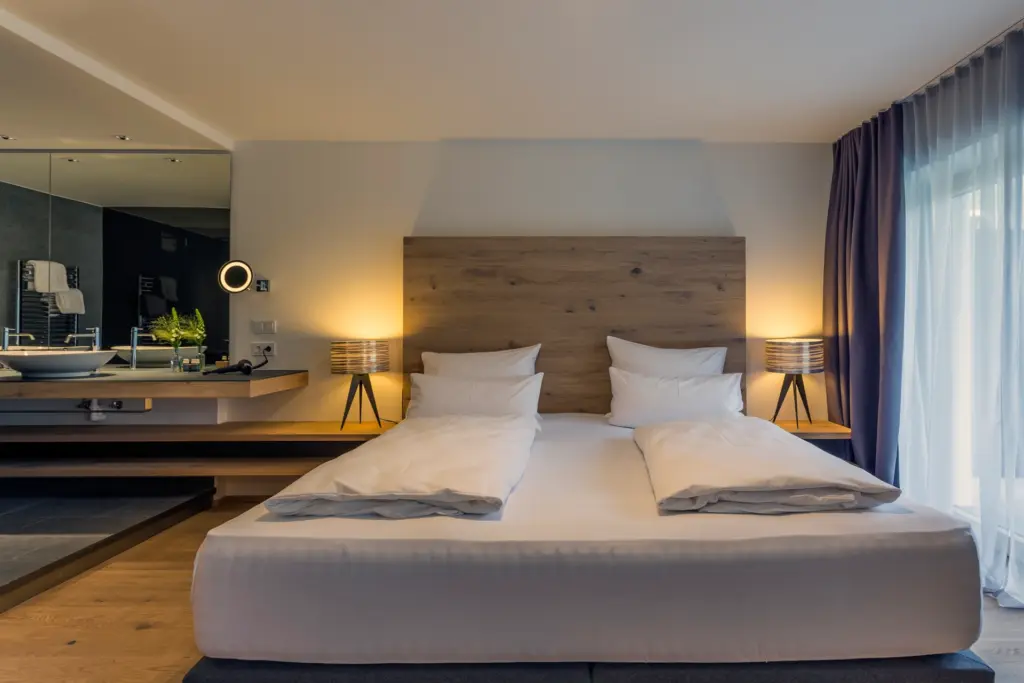 Basic-Zimmer mit viel Altholz und offenem Walk-In-Badezimmer. Bereits die einfachste Zimmerkategorie dieses bei Fenners Reisen buchbaren Wellnesshotels beweist Stil und Komfort.