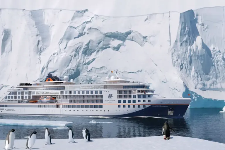 Ein Schiff der Hapag Lloyd Cruises zwischen Gletscher und Pinguinen in der Antarktis - ein besonderes Abenteuer, das bei Fenners Reisen exklusiv gebucht werden kann