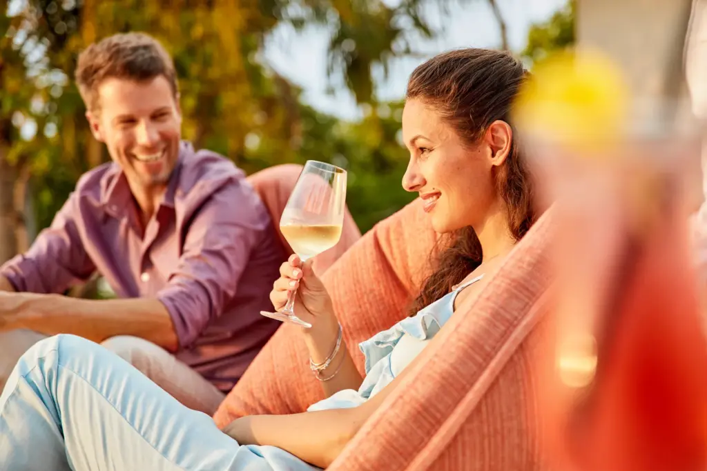 Gesellige Stunden am Strand - eine Frau genießt das gute Gespräch bei einem Glas Wein. Der ROBINSON Urlaub hat für jedes Bedürfnis etwas zu bieten, hier wartet Sport und Entspannung, Ruhe und Geselligkeit. Wonach sehnen Sie sich? Katharina Fenners gestaltet Ihren perfekten Cluburlaub!