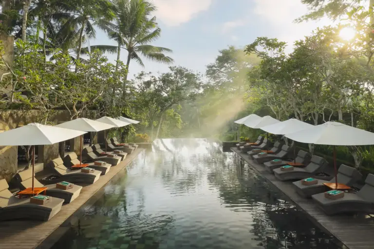 Ein von Liegen, Sonnenschirmen und tropischem Grün flankierter Pool, in dem sich die Sonne spiegelt - stilvolle Zimmer in privaten Villen, ein preisgekröntes Spa und ein überzeugendes Konzept zur Nachhaltigkeit erwarten Gäste in diesem spektakulär gelegenen Resort in Bali. Buchbar für einen unvergesslichen 5-Sterne-Urlaub bei Fenners Reisen!