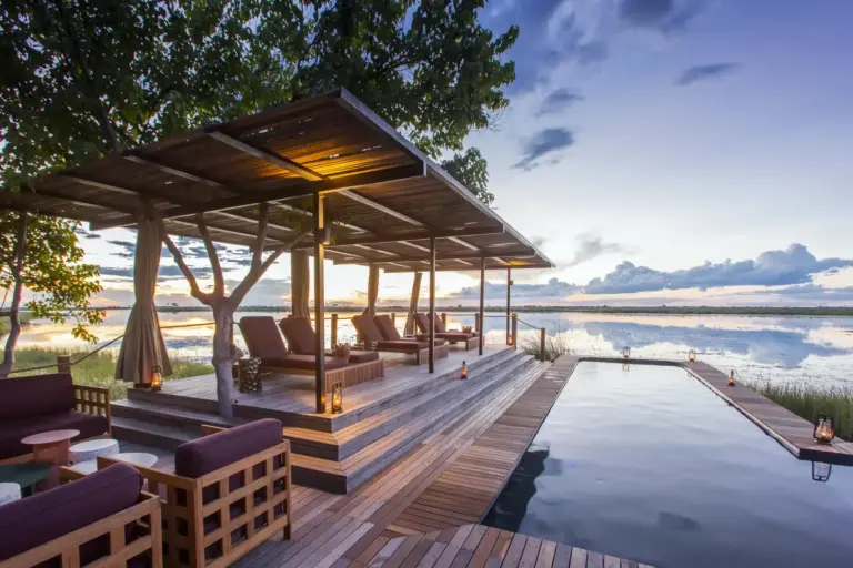 Ein Infinity Pool mit Liegen vor dem Hintergrund afrikanischer Feuchtgebiete. Große Elefantenherden und packende Raubtiersichtungen verspricht der Aufenthalt, individuell buchbar bei der Botswana-Expertin Katharina Fenners.