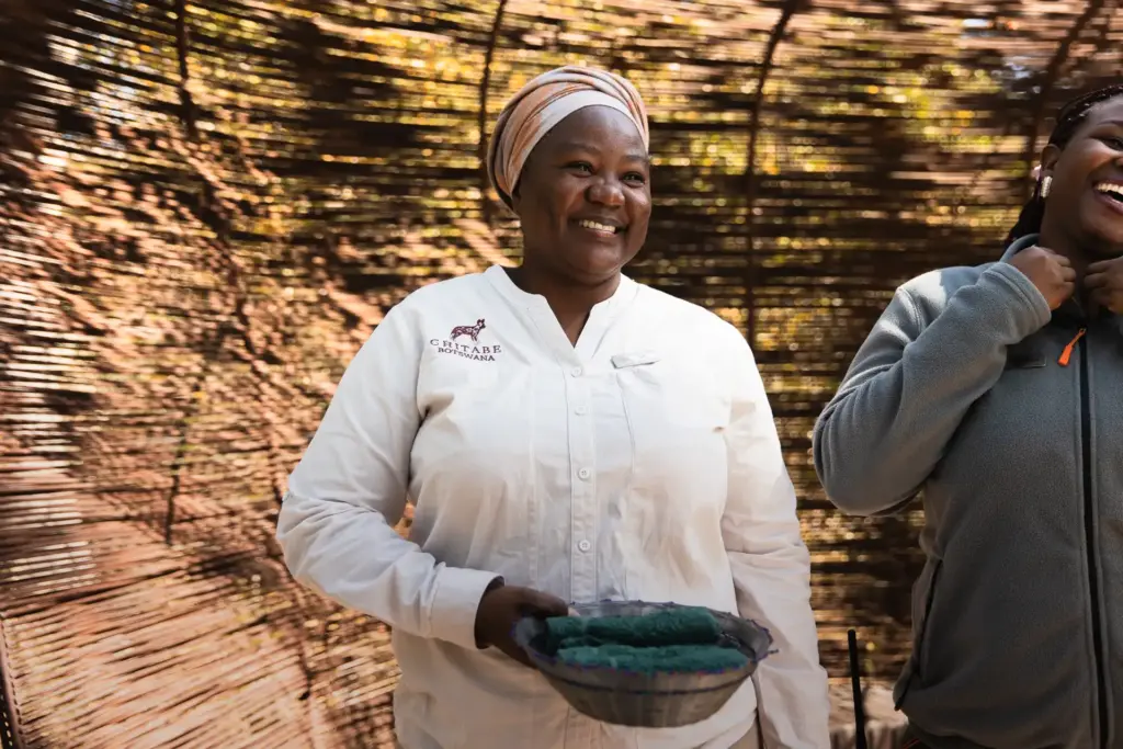 Eine Mitarbeiterin eines der preisgekrönten Wilderness Camps in Botswana hält eine Schale in Händen und strahlt - buchen Sie einen Botswana Safari Urlaub mit Aufenthalten in außergewöhnlichen Lodges und Camps bei Fenners Reisen!