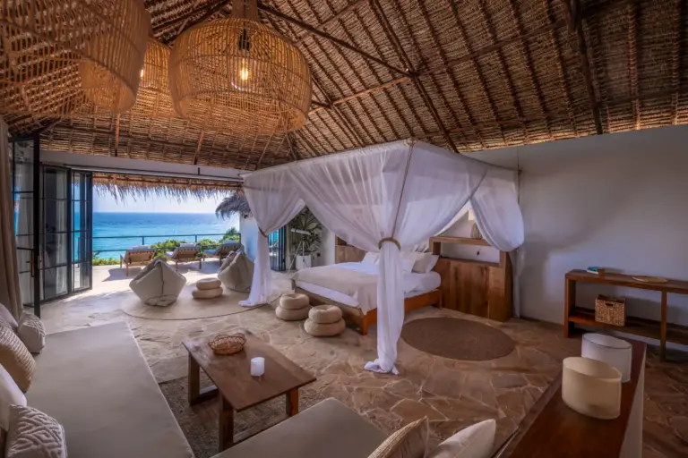 Natürliche Materialien, hohe Decken aus Stroh und viel Stoff prägen dieses luftige Schlafzimmer mit Blick auf den Strand von Pemba Island. Katharina Fenners plant Ihren Aufenthalt im exquisiten The Manta Resort im Rahmen Ihrer Tansania Rundreise.