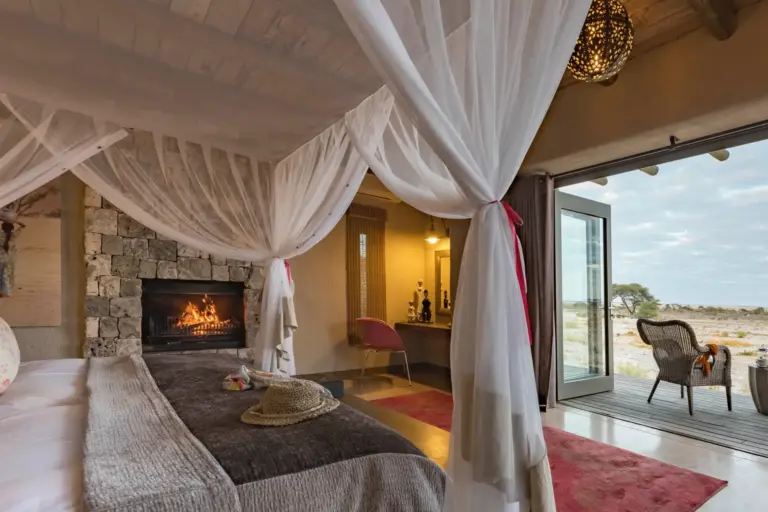 Schlafzimmer mit urigem Kamin und Blick auf die Natur Namibias - das markane Onguma The Fort kann bei Fenners Reisen gebucht werden, individuell oder auch im Rahmen einer maßgeschneiderten Namibia Rundreise.