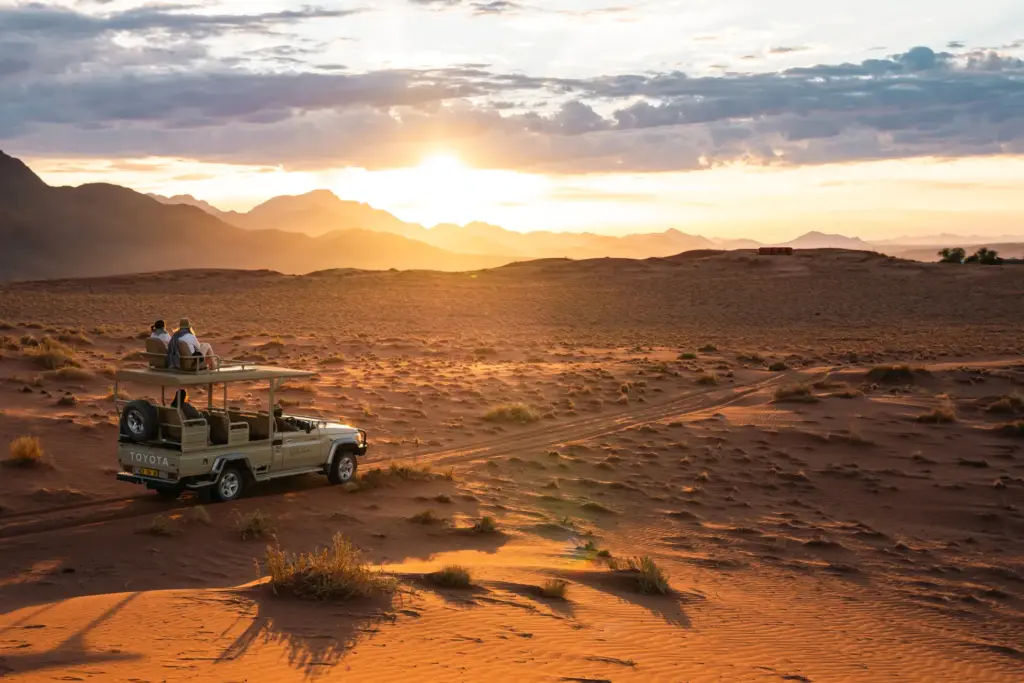 Allrad-Fahrzeug mit Sitzen auf dem Dach in der namibischen Wüste bei Sonnenuntergang. Katharina Fenners arrangiert Ihr individuelles Namibia Wüsten-Erlebnis, ob im Jeep, auf Pferderücken oder auf dem Bike! Jetzt individuell beraten lassen.