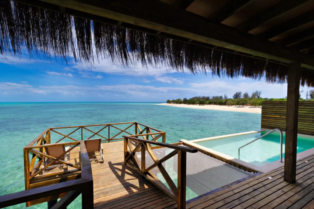 Terrasse und Infinity Pool einer Wasservilla mit Blick auf den türkisblauen Ozean vor Bawe Island Zanzibar. Der Aufenthalt auf der exquisiten Privatinsel kann individuell bei Fenners Reisen gebucht werden, auch in Verbindung mit einer Tansania Safari!