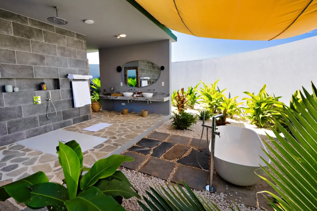 Luxusiöses Outdoorbadezimmer mit großer, bodentiefer Regendusche und freistehender Wanne zwischen tropischem Grün - in diesem Luxusresort auf Sansibar stimmt jedes Detail. Katharina Fenners plant Ihren individuellen Sansibar Luxusurlaub!