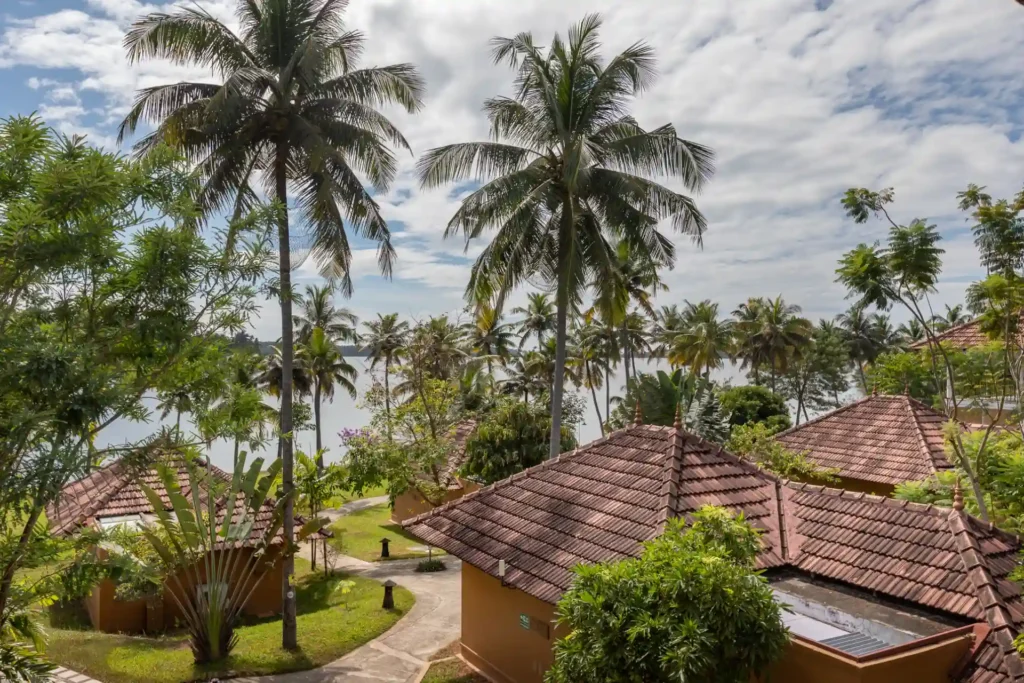 Mehrere Gebäude schmiegen sich unter Palmen ruhig an einen See. Wer einen nachhaltigen Gesundheitsurlaub plant, findet in dieser indischen Ayurvedaklinik ganzheitliche Regeneration. Katharina Fenners ist Expertin für Wellness- und Gesundheitsreisen weltweit und berät Sie individuell!