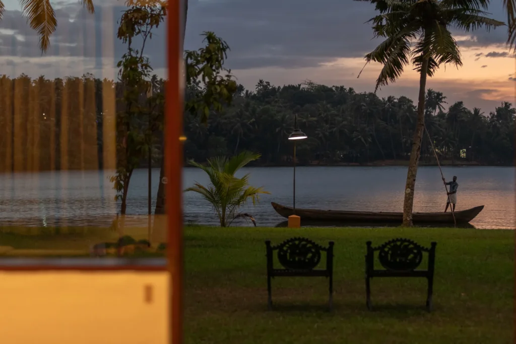 Blick auf zwei Stühle, ein Boot und den See in der Abenddämmerung, aus einem der Zimmer der Kalari Rasayana Ayurvedaklinik. Buchen Sie eine maßgeschneiderte Gesundheitsreise nach Indien bei der Expertin Katharina Fenners!