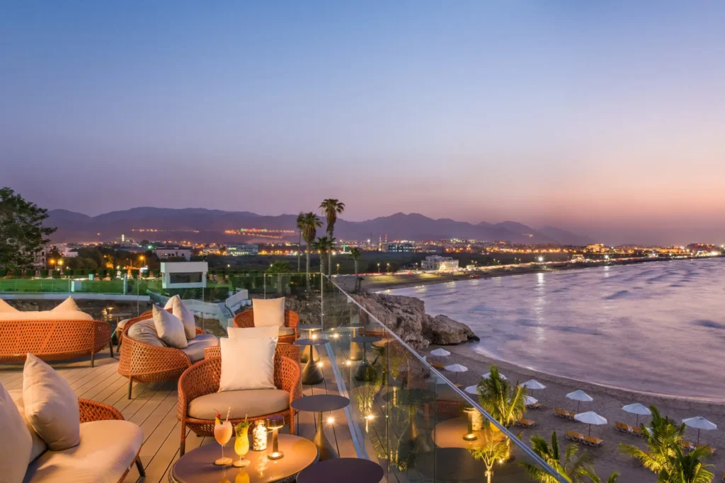 Abendstimmung in einer Rooftop Bar mit Blick über eine glitzernde Bucht - eine Reise in den Oman bietet Luxus und Abenteuer! Buchen Sie Ihren Oman Urlaub individuell bei Katharina Fenners!