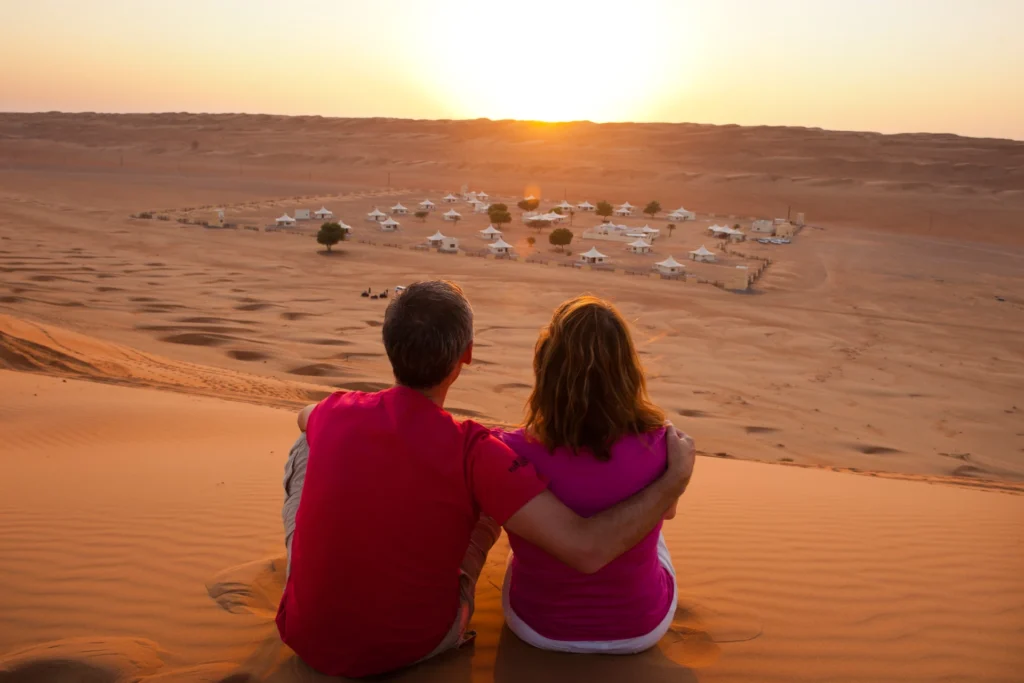 Ein Paar genießt den Sonnenuntergang über einem Wüstencamp in der Wüste Wahiba Sands, ein Highlight jeder Oman Rundreise. Buchen Sie einen unvergesslichen Oman Urlaub bei Fenners Reisen!