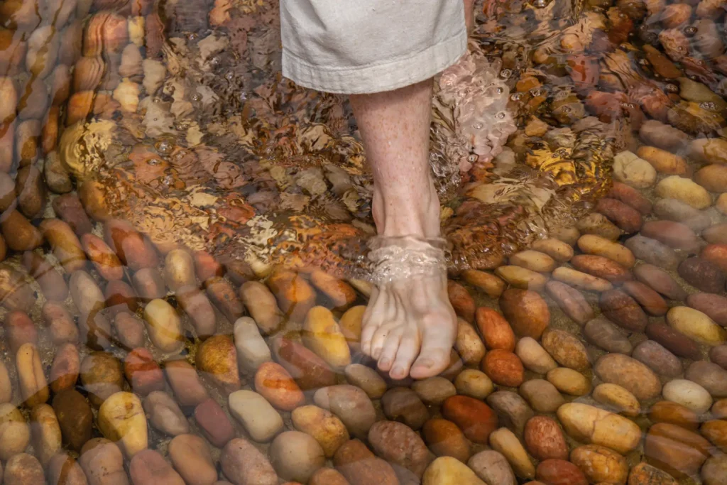 Füße auf großen Kieseln im Wasser - der Gesundheitsurlaub im Praktiki Shakti ist eine ganzheitliche, sensorische Erfahrung, buchbar bei der Wellness-Expertin Katharina Fenners.
