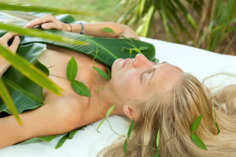 Eine Frau, bedeckt von grünen Blättern - im Longevity-Retreat Prakriti Shakti geht es um nachhaltige Heilung im Einklang mit der Natur. Buchbar ist der regenerierende Aufenthalt bei Fenners Reisen.