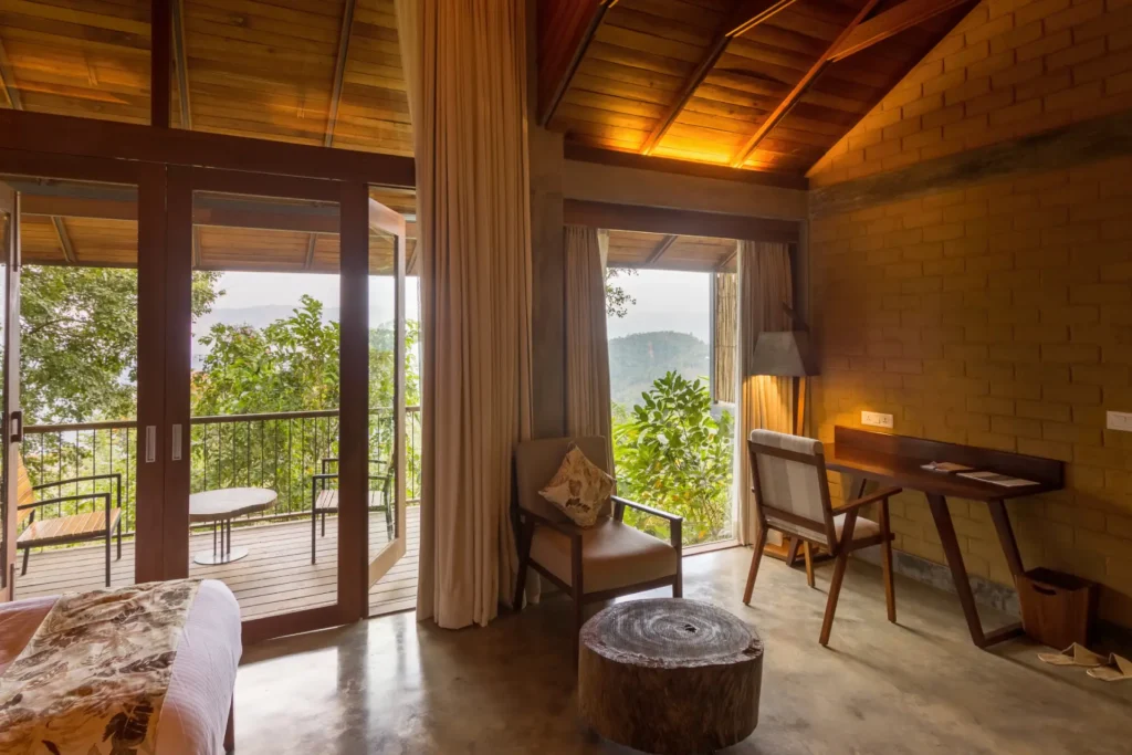 Schlafzimmer des Praktiki Shakti Gesundheitsresorts mit Schreibtisch und Balkon, von dem der Blick ins Grüne schweifen darf, buchbar bei Fenners Reisen.