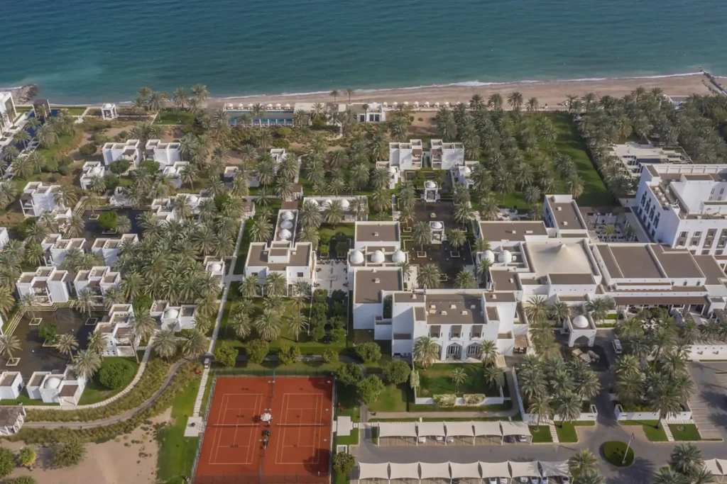 Blick über das weitläufige The Chedi Muscat am Oman. Die niedrigen, architektonisch raffinierten Gebäude schmiegen sich in einen großen Garten voller Wasser und Pools direkt am Meer. Buchen Sie eine unvergessliche Oman Reise bei Fenners Reisen!