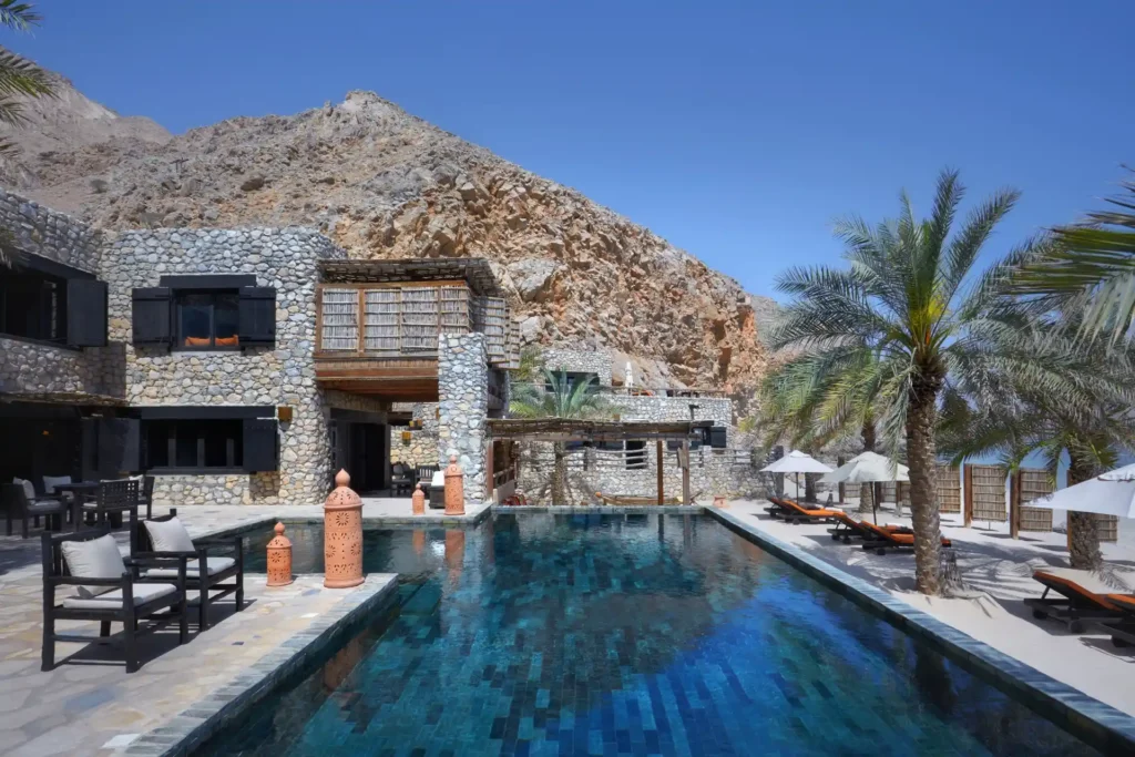 Ein großer Pool vor einer steinernen Villa in omanischem Stil - bis zu zehn Gäste genießen exklusive Privatsphäre in dieser omanischen Villa am Strand, buchbar bei Fenners Reisen.