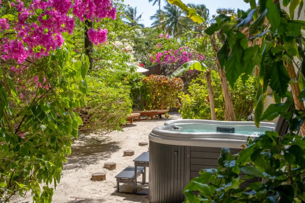 Der Whirlpool der Cinnamon-Doppelzimmer des Zanzibar White Sand Resorts liegt idyllisch im Garten, umrahmt von rosa Blüten. Buchen Sie einen unvergesslichen Sansibar Urlaub bei der Expertin Katharina Fenners!