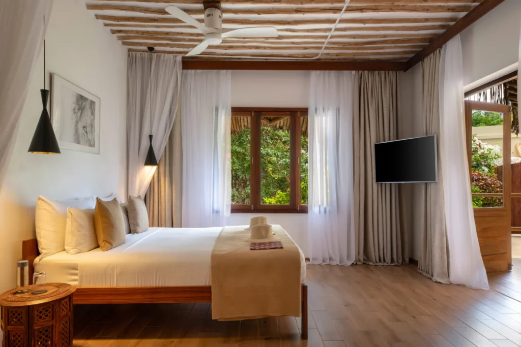 Holz, Luftige Vorhänge und stilvolle Pendelleuchten machen dieses Cinnamon-Doppelzimmer eines Luxusresorts auf Sansibar so besonders. Individuell buchbar für einen exklusiven Urlaub auf Sansibar oder eine Sansibar-Tansania-Kombinationsreise bei Fenners Reisen!
