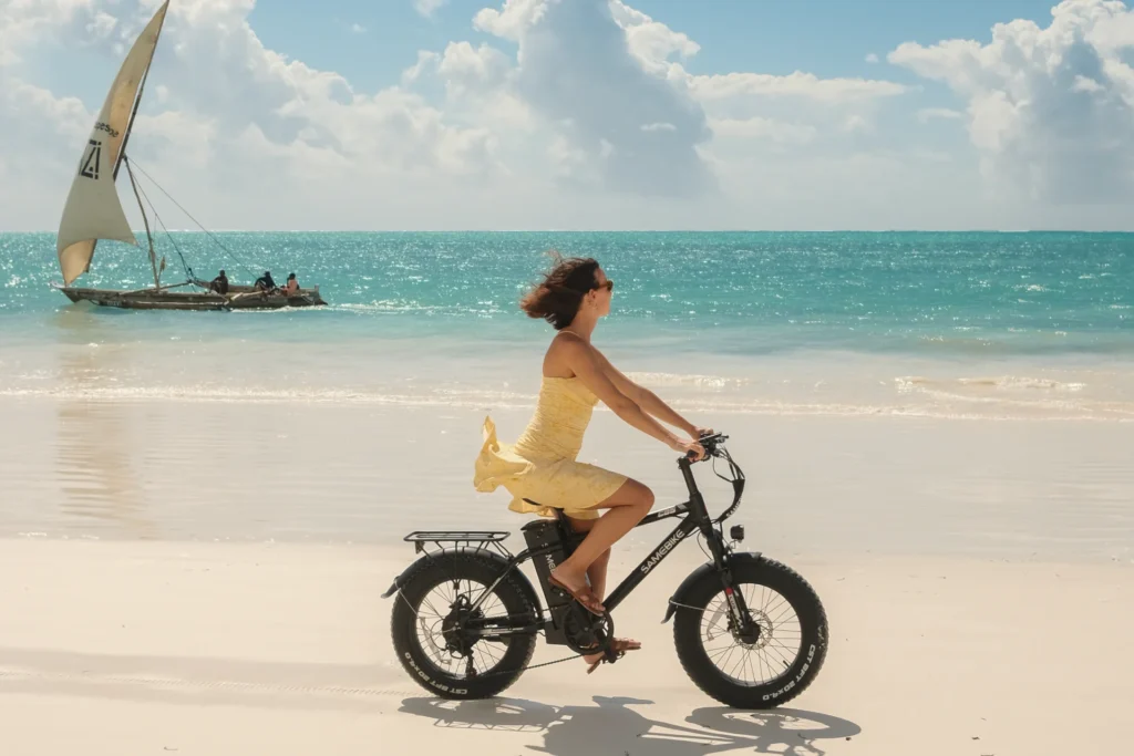 Eine Frau in sommerlichem Kleid radelt auf einem E-Bike den Bilderbuchstrand Sansibars entlang. Sie möchten Sansibar entdecken? Katharina Fenners plant Ihren Urlaub auf Sansibar individuell - auch in Kombination mit einer Reise nach Tansania.