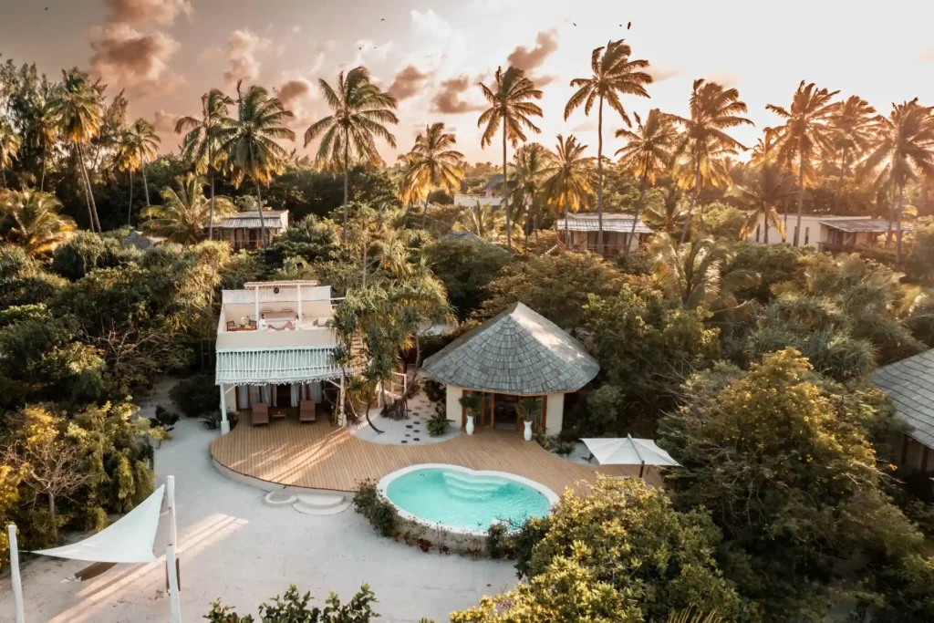 Blick aus der Luft auf eine geräumige Strandvilla mit einem Schlafzimmer, umrahmt von weißem Sand und Palmen. Die Villa liegt an einem Bilderbuchstrand auf Sansibar und kann für Ihre individuelle Sansibar Reise bei uns gebucht werden.