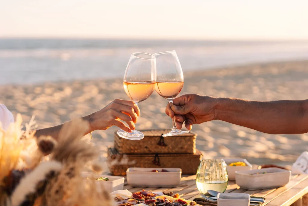 Ein Paar stößt mit Weißwein an, im Hintergrund ein Picknick an einem leeren Sandstrand im südlichen Portugal. Gehobene Kulinarik, eine facettenreiche Kultur und stimmungsvolle Landschaften machen den Portugalurlaub zu einem Erlebnis voller Luxus, abgerundet durch erstklassige Hotels. Katharina Fenners berät Sie individuell!