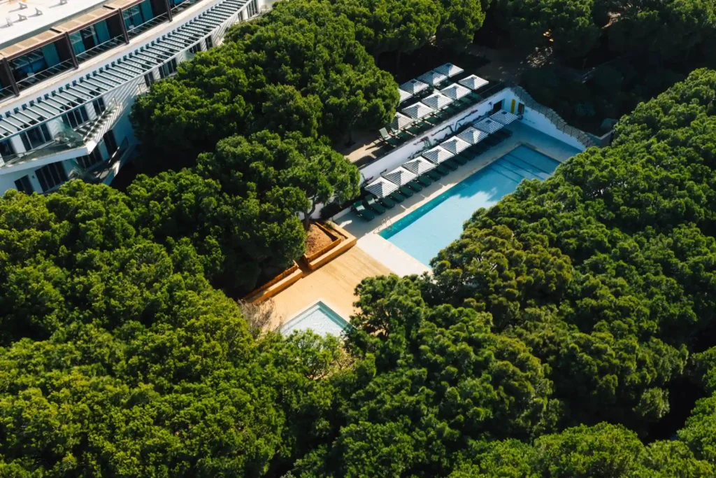 Blick aus der Luft auf den von dichten Pinien umrahmten Pool des Octant Praia Verde. Das Hotel ist buchbar für Ihren individuellen Portugalurlaub bei der Expertin Katharina Fenners!