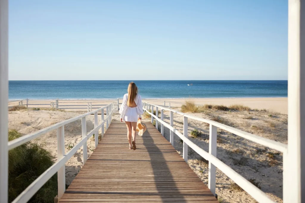 Eine Frau spaziert über einen Steg zum leeren Strand. Die Praia Verde in Portugal zählt zu den schönsten und ruhigsten Strandabschnitten der Ostalgarve. Katharina Fenners kennt die besten Hotels und gestaltet Ihren Aufenthalt individuell!