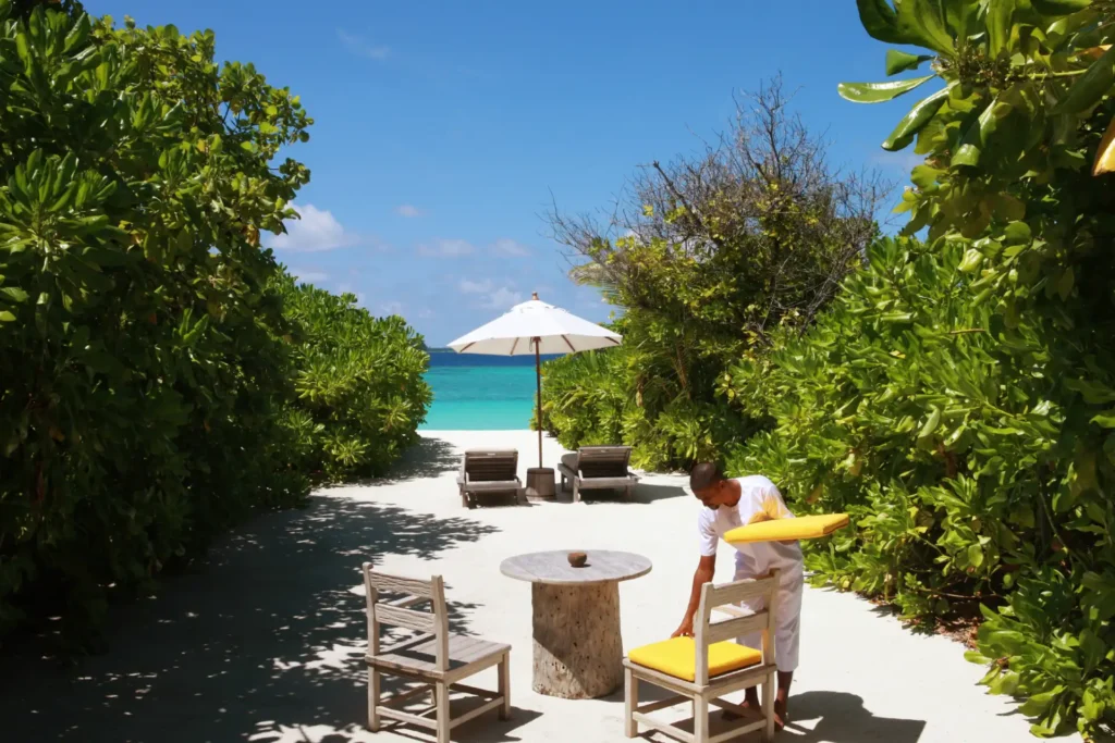 Ein Butler platziert die Kissen am privaten Strandabschnitt einer maledivischen Insel. Die Villa kann individuell bei Fenners Reisen gebucht werden!