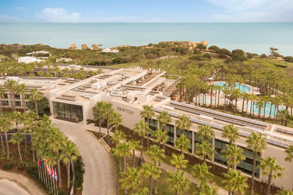 Blick aus der Luft auf das Designhotel Kimpton Atlantico Algarve, umrahmt von einer grünen Gartenanlage, im Hintergrund das Meer. Buchbar für einen erstklassigen Portugalurlaub bei Fenners Reisen!