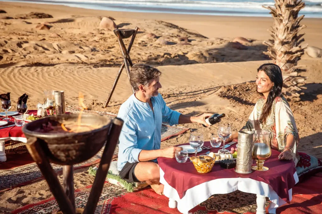 Ein Paar genießt ein marokkanisches Dinner zwischen Dünen und Palmen am Strand von Agadir. Buchen Sie ausgezeichneten Cluburlaub in Marokko bei Fenners Reisen!