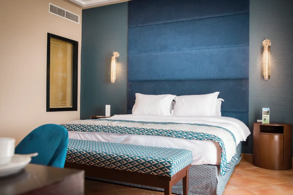 Gedecktes Blau und Erdtöne prägen dieses marokkanisch inspirierte Hotelzimmer am Sandstrand von Agadir. Buchen Sie einen individuellen Cluburlaub bei Fenners Reisen!
