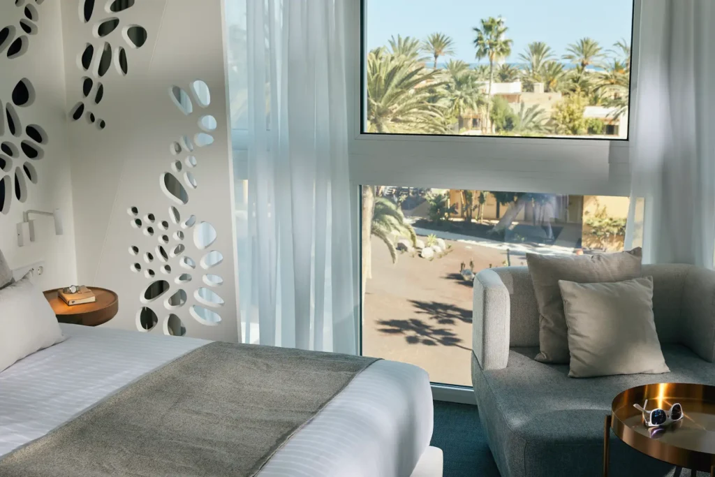 Modernes Zimmer mit weißem Mobiliar und Blick auf die stilvolle Clubanlage des ROBINSON Jandia Playa. Das Zimmer kann bei Fenners Reisen gebucht werden.