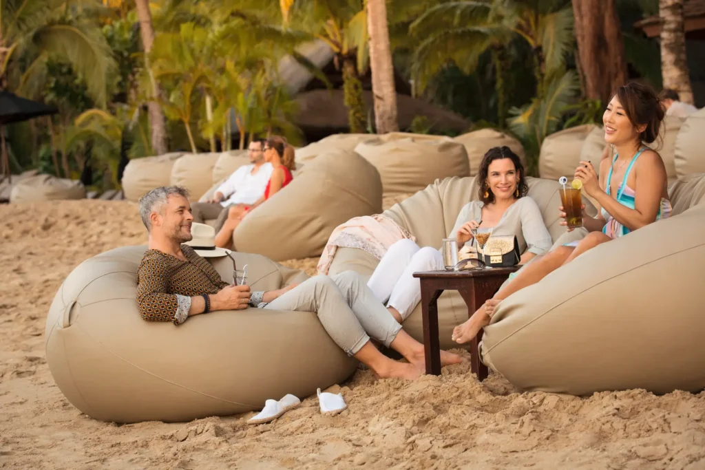Fröhliche Menschen entspannen in Sitzsäcken am wunderschönen Strand des ROBINSON Khao Lak. Der Aufenthalt kann individuell bei Fenners Reisen gebucht werden.