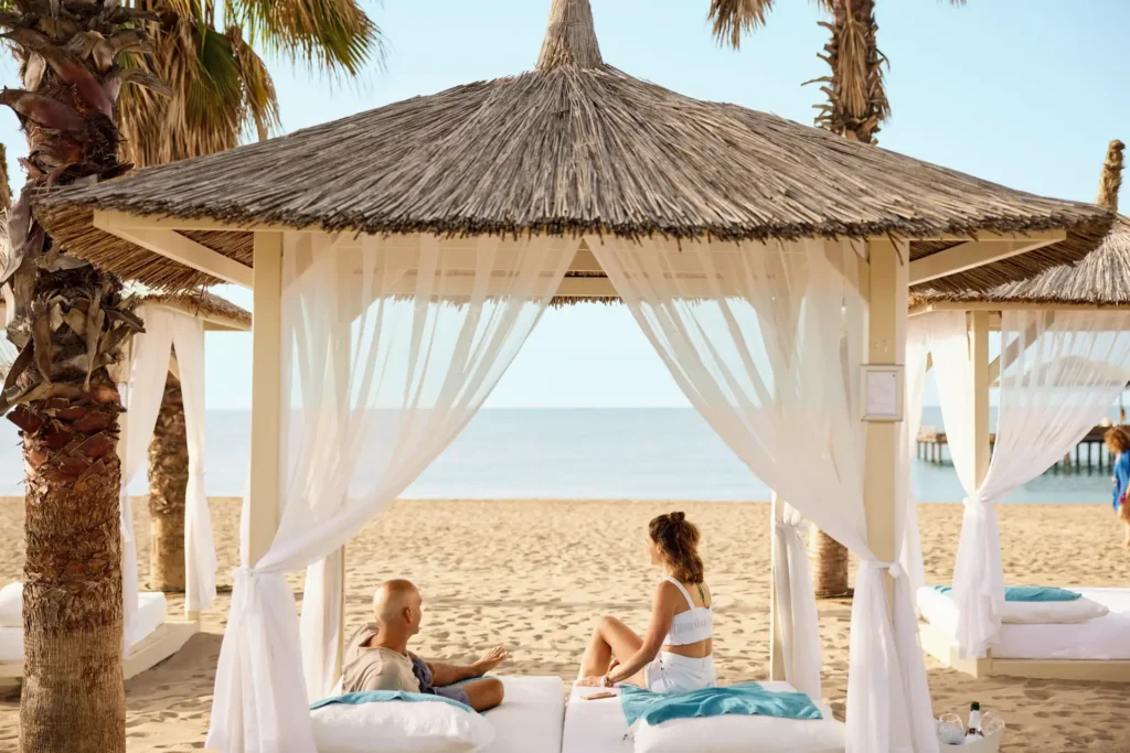 Ein Paar auf einem Balibed am Strand vor dem ROBINSON Nobilis in der Türkei. Der Aufenthalt in diesem hervorragenden Clubresort kann individuell bei Fenners Reisen gebucht werden.