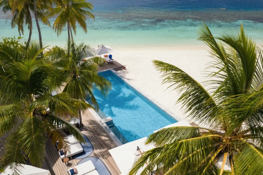 Pool unter Palmen an einem strahlend weißen Strand - die Kulisse des V Villas Maldives at Mirihi ist traumhaft. Perfekt für einen intimen Malediven Luxusurlaub, individuell buchbar bei Fenners Reisen