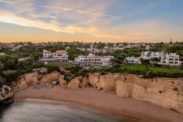 Das Luxusresort Vila Vita Parc im Abendlicht - direkt über der ikonischen Felsküste der Algarve, mit weitem Sandstrand und rosa schimmerndem Meer. Buchen Sie einen individuellen Aufenthalt bei Fenners Reisen!
