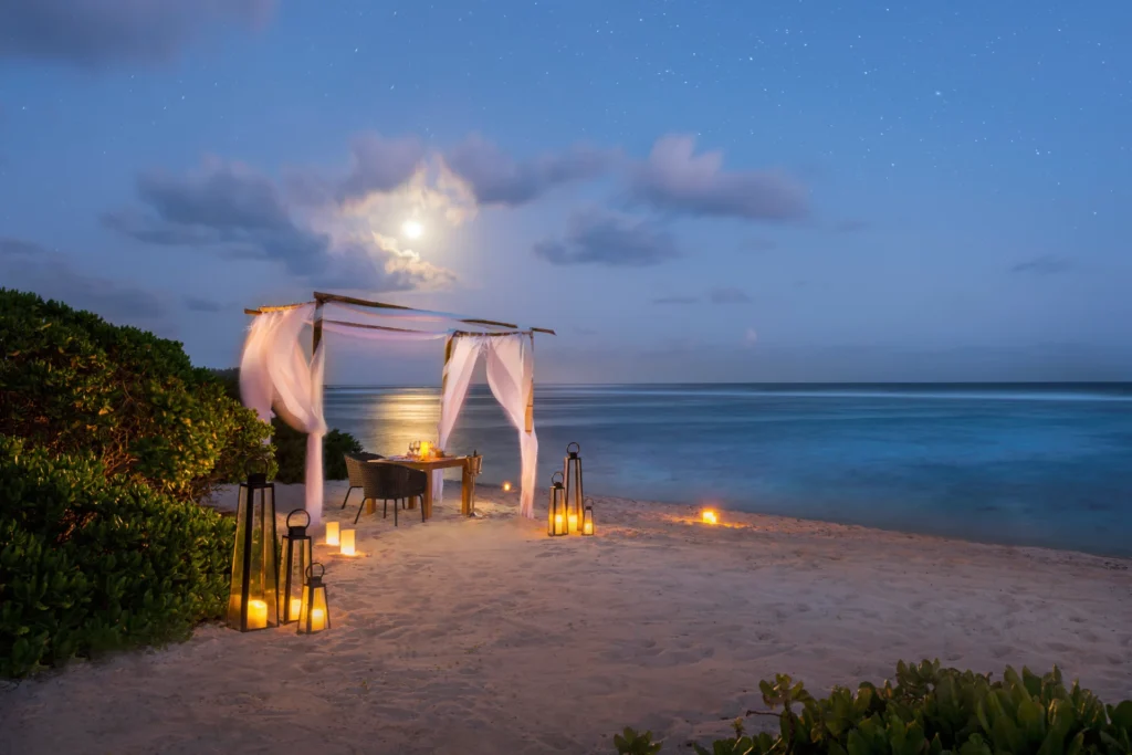 Romantischer Tisch im Abendlicht am Strand - Barfuß-Dinner versprechen knisternde Romantik im Constance Le Chaland Mauritius. Buchen Sie unvergessliche Mauritius Flitterwochen bei Fenners Reisen!