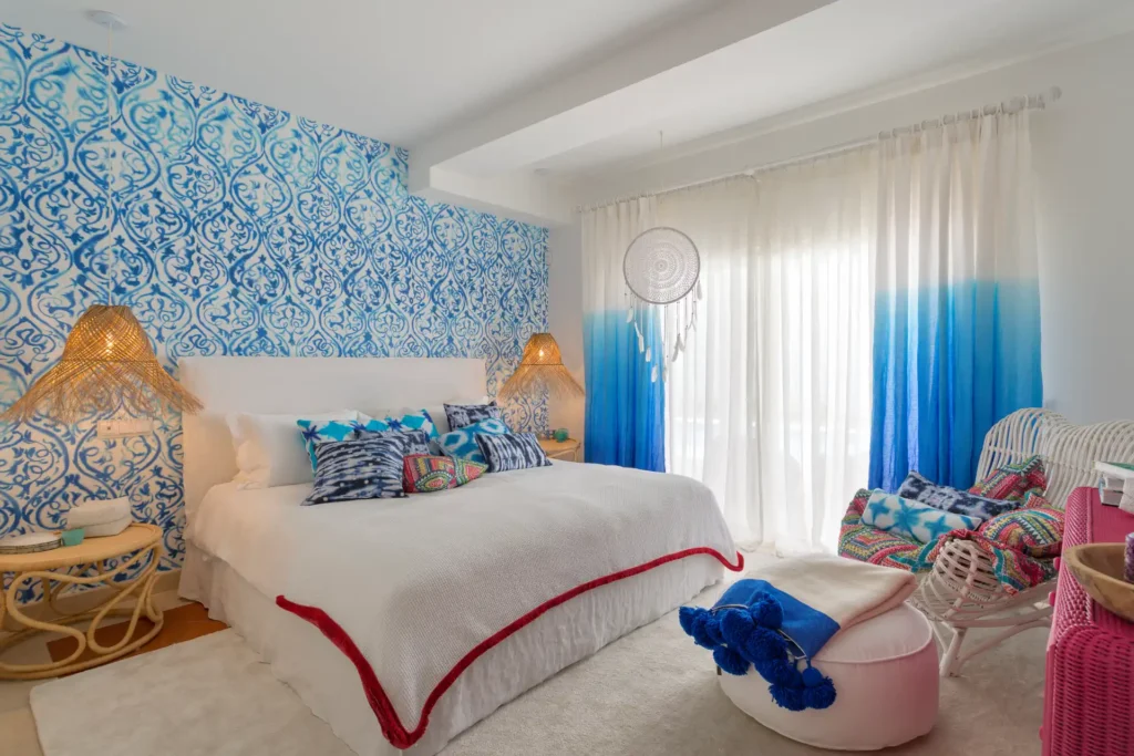 Bunt gemusterte Tapeten, Teppiche und Rattanmöbel im Boho-Chic verzieren dieses Schlafzimmer der Villa Hibiscus Beach House an der Algarve. Jetzt Ihre Traumvilla in Portugal bei Fenners Reisen buchen!