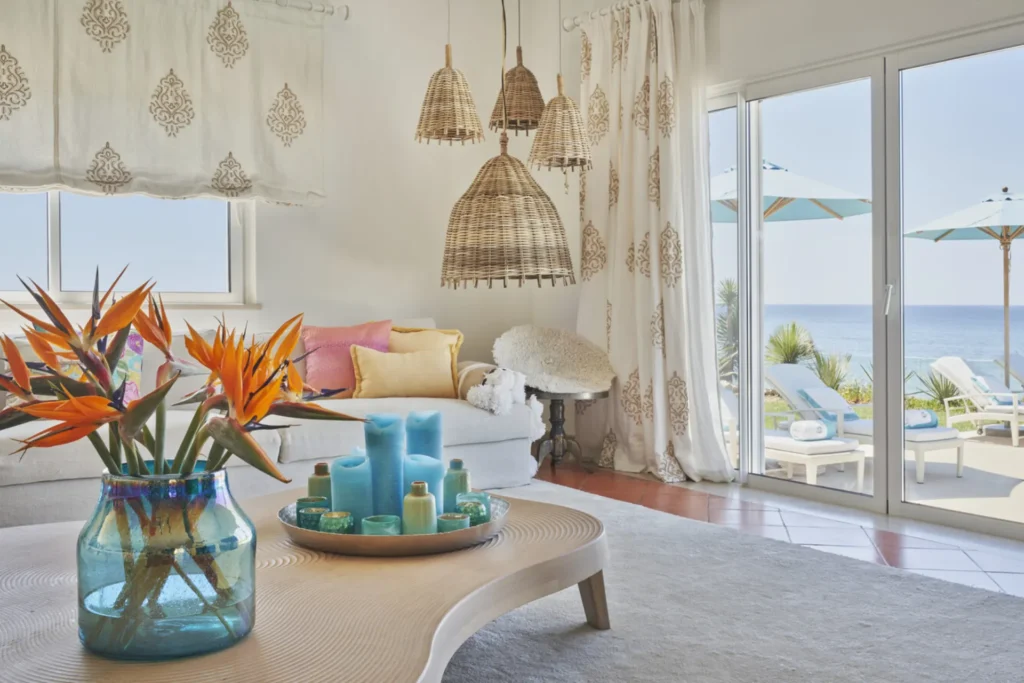 Strelitzien im Glas, Hängeleuchten und ein weiter Blick übers Meer zeichnen das lichtdurchflutete Wohnzimmer der Villa Hibiscus Beach House aus - jetzt individuell bei Fenners Reisen mieten!
