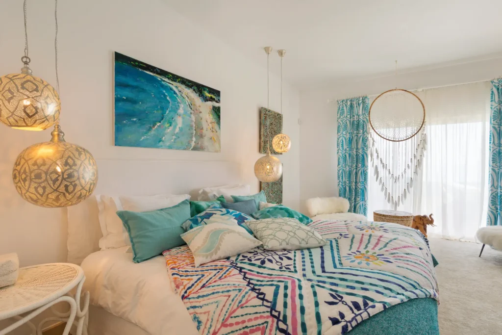Hängeleuchten, knallige Kunst und bunte Plaids machen dieses Schlafzimmer einer portugiesischen Strandvilla zur oplulenten Augenweide. Die Villa an der Algarve ist individuell bei Fenners Reisen buchbar!
