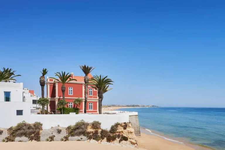 Blick aus der Ferne auf die rote Fassade der historischen Prunkvilla Red Chalet an der Algarve. Sie möchten eine Strandvilla in Portugal mieten? Katharina Fenners berät Sie persönlich!
